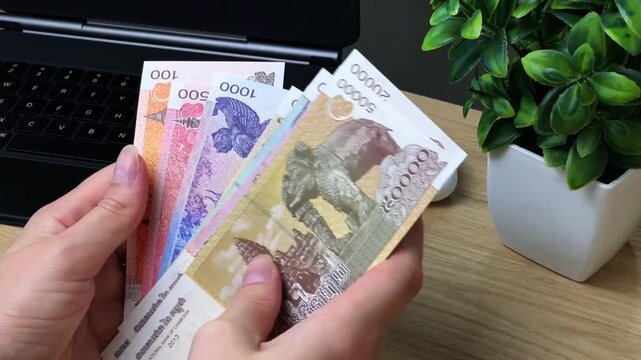 A close-up of a woman counting Cambodian riel banknotes at her desk. Conceptual concepts of finance, money management, budgeting, and income.