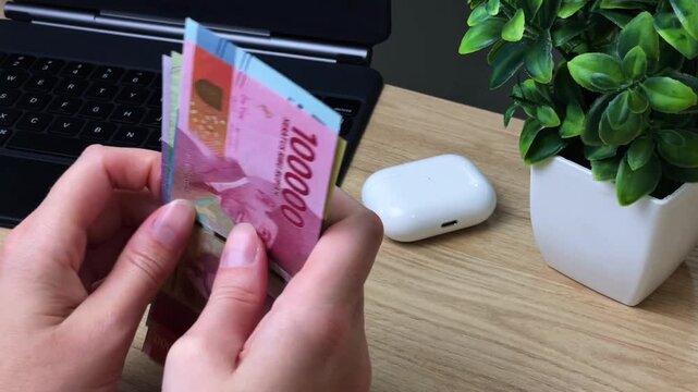 A woman sorts through Indonesian rupiah banknotes at her desk. Concepts for travel, currency exchange, spending abroad, and financial planning.