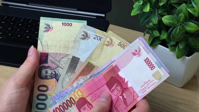 A woman sorts through Indonesian rupiah banknotes of various denominations at her desk. Concept of financial control, budgeting, and cash accounting.