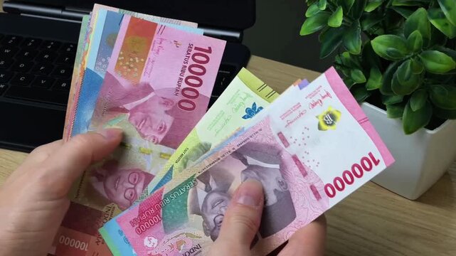 A close-up of hands sorting through Indonesian banknotes of various denominations in three different styles. Conceptual references to collecting, numismatics, currency diversity.
