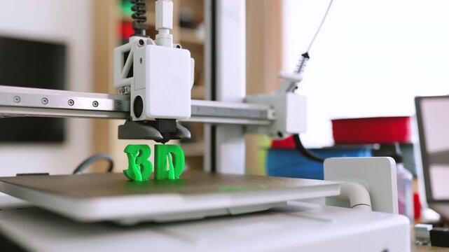 A modern 3D printer is actively creating green plastic letters on its build plate with a laptop displaying the 3D logo in the background