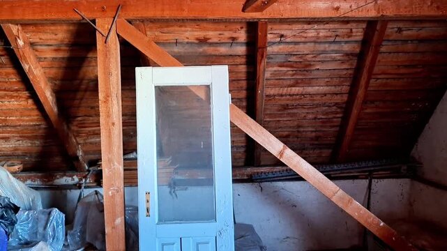 Attic space with slanted wooden ceiling, white door, stools, and stored items, capturing a rustic storage area filled with household belongings and vintage atmosphere
