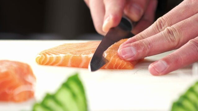 Professional chef slicing fresh raw salmon on a white cutting board