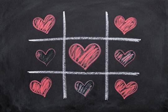 A tic tac toe game with red hearts on a black surface