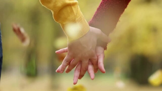 Lovely shot of a Romantic couple holding hands in a sunset park. interlocking fingers with autumn background with falling leaves and warm yellow tones.