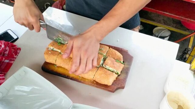 Chef slicing crispy Martabak Telur savory pancake with a large cleaver on a wooden board.