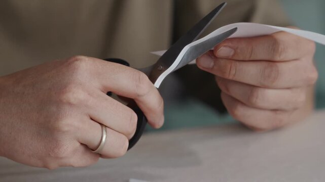 Close-up of hands holding scissors after cutting a sheet of white paper. The blades open slightly while the paper piece is already separated on the table. High quality 4k footage