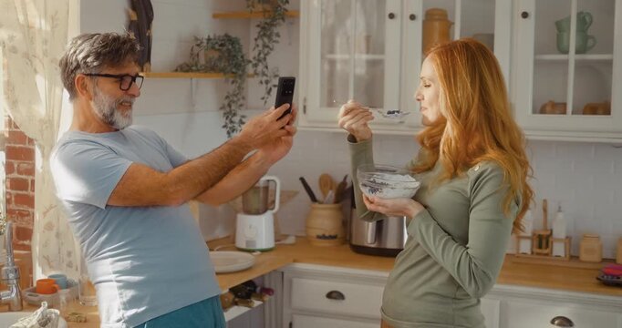Happy mature couple taking selfie while enjoying healthy breakfast at home. Morning lifestyle, love, relaxation and bonding in cozy kitchen.
