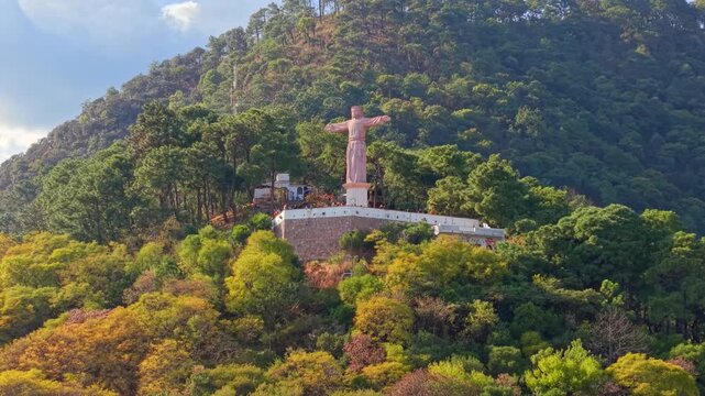 Aerial orbit establishing shot of the monumental Christ of Taxco surrounded by greenery on Atachi Hill in the state of Guerrero, Mexico, on a sunny day, high frame rate.