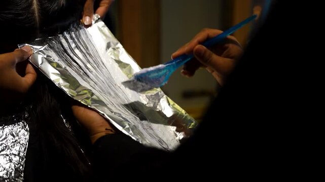 Hairdresser applies dye with brush onto hair section placed on aluminum foil during salon treatment