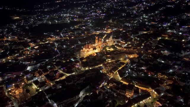 Panoramic aerial view at night of the city of Taxco de Alarcon in Guerrero, Mexico, with the Santa Prisca temple in the center, streets illuminated with colonial architecture.