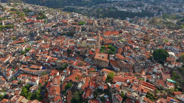 Establishing panoramic aerial view of Taxco de Alarcon, Guerrero, Mexico, and the Santa Prisca church at sunset, with colonial architecture and orange tile roofs.