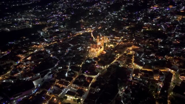 Flying over Taxco at night with illuminated streets and the Santa Prisca temple in the center of the city in Guerrero, Mexico