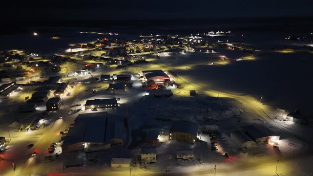 Rankin Inlet, Nunavut Arctic town at night with illuminated houses, streets, and downtown buildings glowing across the snowy northern community along the Hudson Bay coastline under dark skies.