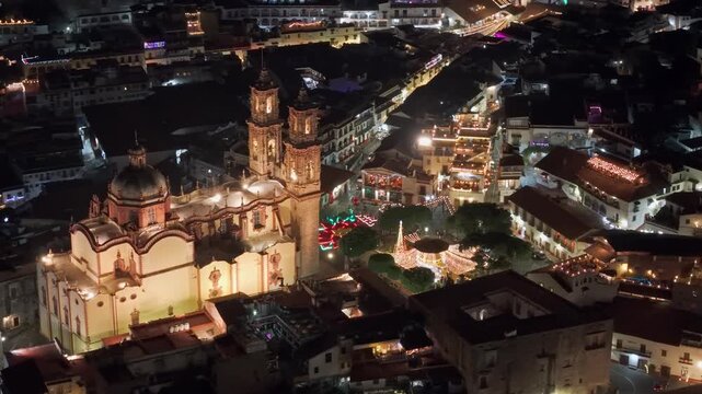 Bird's-eye view of the parish church of Santa Prisca at night in the city of Taxco with warm lighting, main square and illuminated streets, surrounded by white colonial houses, Guerrero, Mexico