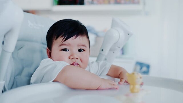 4K slow motion footage of an Asian mother feeding her six month old baby boy with a spoon. Tender parenting moment showing care, bonding, and infant nutrition in a warm home environment.	
