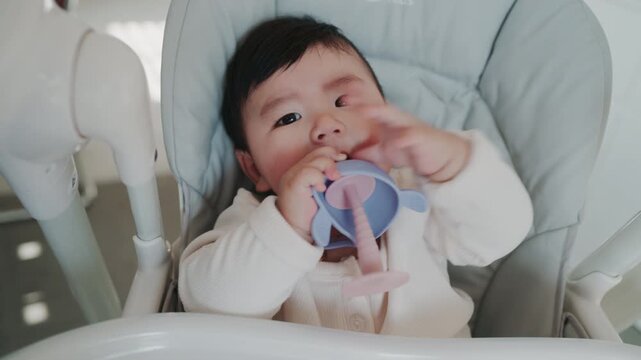 4K slow motion footage of an Asian mother feeding her six month old baby boy with a spoon. Tender parenting moment showing care, bonding, and infant nutrition in a warm home environment