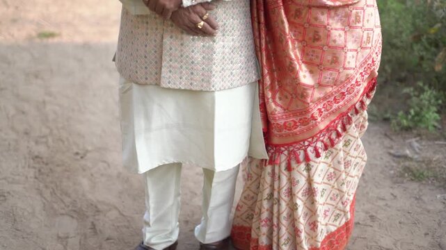 Elderly Indian Couple in Traditional Wedding Attire Standing Together Outdoors - Close-up of Senior Man in Kurta and Woman in Patterned Silk Saree with Tassels