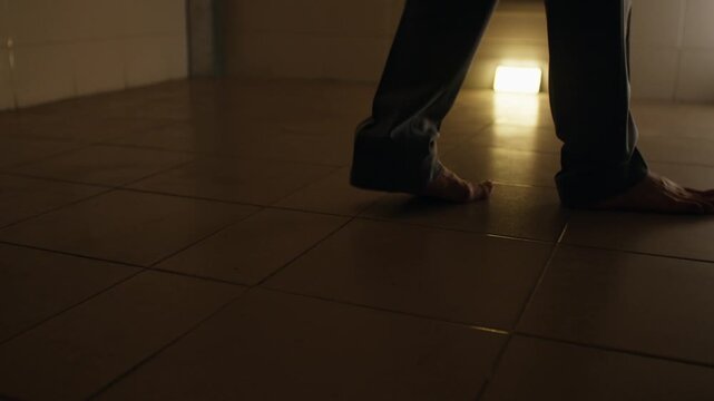 Barefoot man pacing in dimly lit cell, evoking solitude and tension