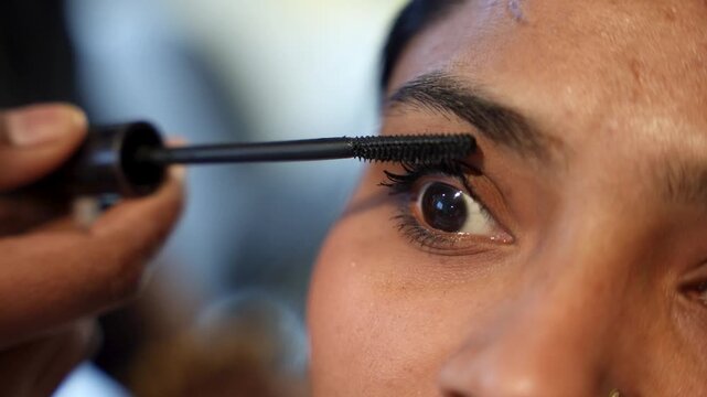 A makeup artist carefully applies black mascara to the lower lashes of a client&rsquo;s eye