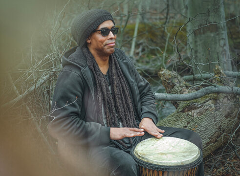 A man with dreadlocks plays the djembe in the forest