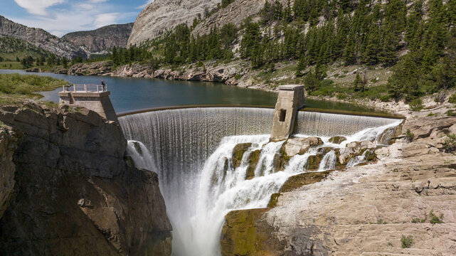 Water flows over a tall dam in a narrow mountain valley.