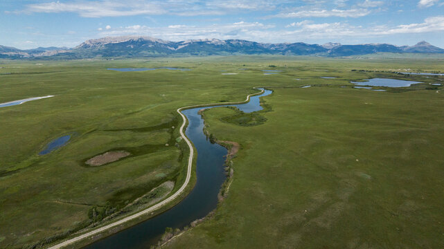 Aerial shot of a meandering river in green meadows with mountains