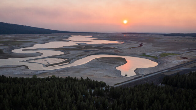 River path courses through dry reservoir at sunset. American West.