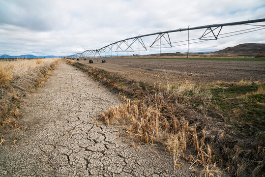 A dry irrigation canal beside a crop field with irrigation pivot