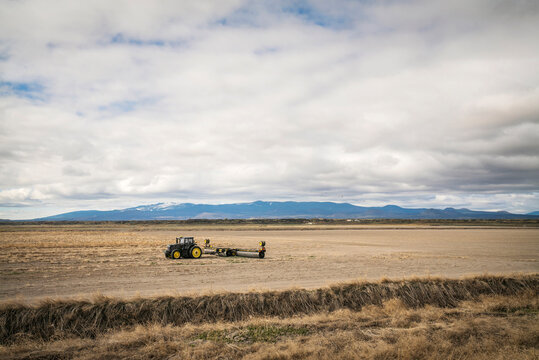 A tractor pulls farm equipment in a dry field.