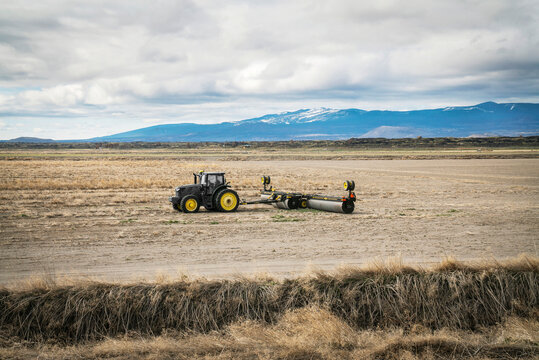 A tractor pulls farm equipment in a dry field.