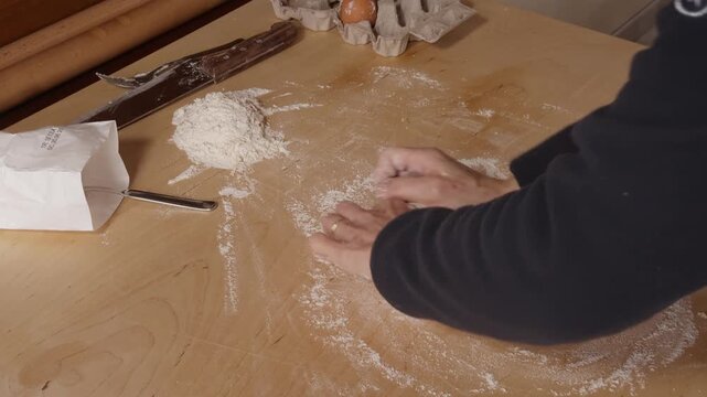 Close-up view of a Romagna cook kneading fresh cappelletti dough by hand on a wooden table. Traditional Italian pasta-making with flour, eggs, and simple kitchen tools.