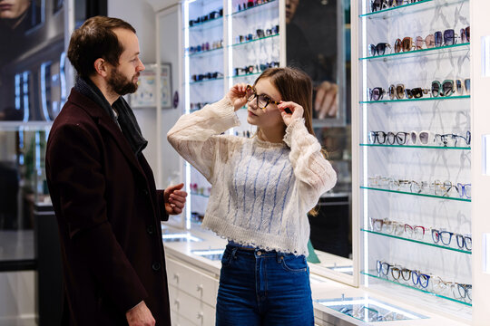 Father and daughter choosing glasses frames in an optician store.