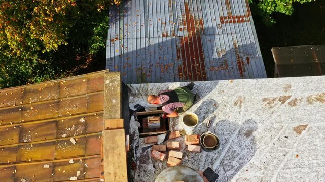 Rooftop chimney construction in progress with tools, bricks, and ventilation cap visible, aerial view