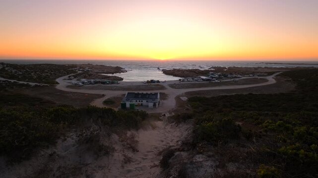 Girl besties run down sandy dune during coastal sunset with view over campsite