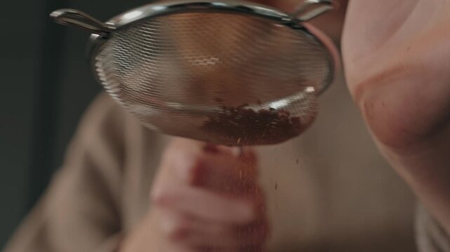 Slow motion cocoa powder falling through sieve by hand