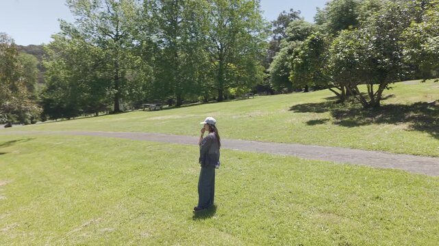 A woman stands on a sunny day at Silvan Reservoir, surrounded by lush green grass and trees. The serene atmosphere and natural beauty create a sense of peace and relaxation.