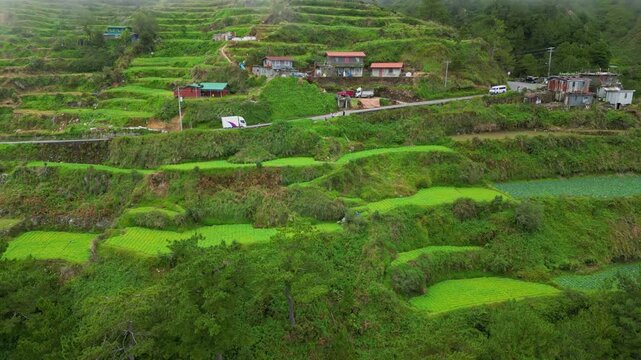 Dynamic right-turning push in aerial toward the clustered rural settlements and winding highway nestled in the heart of Buguias, Benguet, Philippines.