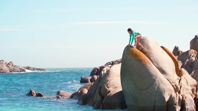 Scared young girl paralysed by fear to jump off coastal rock into ocean
