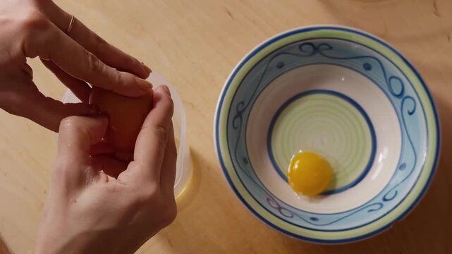A person carefully separates an egg yolk from the white, holding the cracked shell above a bowl and container.