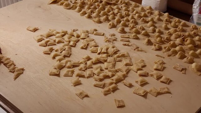 Dozens of ravioli and cappelletti rest on a wooden table, freshly shaped and cut with a pastry wheel.