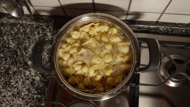 Cappelletti boil in bubbling water inside a stainless pot on a stovetop, seen from above during cooking.