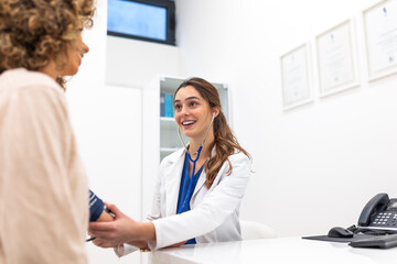 Fototapeta premium Smiling female doctor measuring blood pressure of woman patient in clinic office. Professional practitioner using manual sphygmomanometer. Healthcare and medicine consultation and hypertension concept