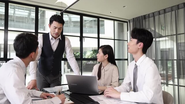 Business co-workers actively communicating and exchanging ideas about work at their desks, attentively listening to a colleague's presentation of financial data and analysis on a laptop screen