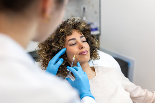 Close up of professional surgeon injecting botox in woman's cheek. Facial rejuvenation, dermal filler treatment concept. Female doctor in gloves performing aesthetic procedure in a medical clinic.