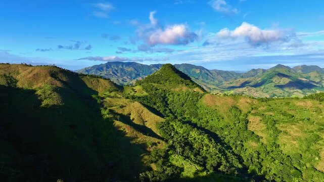 Panoramic view of a sun-drenched mountain range. Wooded foothills under a cloudy sky. A stunning aerial view of the Dominican Republic's tropical mountain landscape. A natural summer mountain scenery.