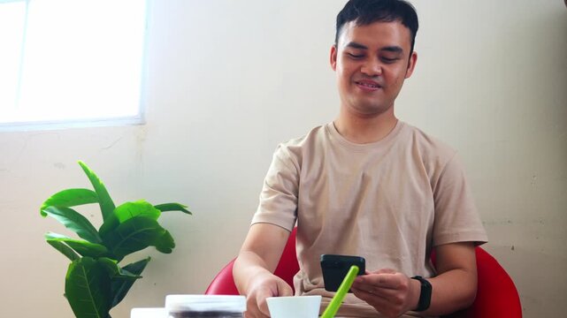 Happy fotografer browsing social media on phone while having hot beverage in room