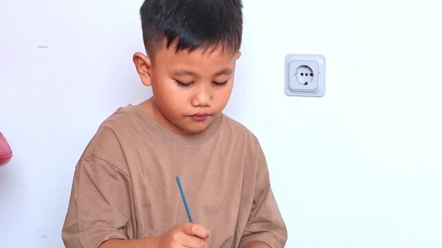 Focused asian boy painting project DIY with brush and paint pallet at home