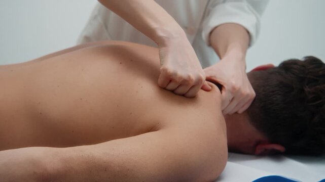 Close-up of hands performing upper back and shoulder massage on a male client in a clinical environment.