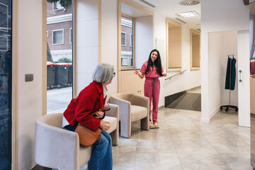 Young medical staff member greeting and talking with an elderly patient in a modern hospital or dental clinic lobby waiting area © Koldo_Studio